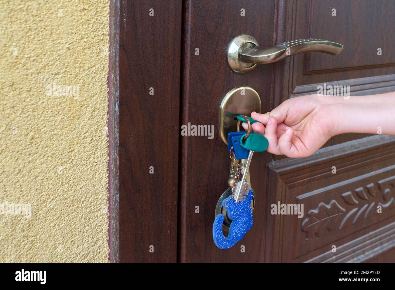 Child's hand unlocking entrance door with a key. Person using keys and