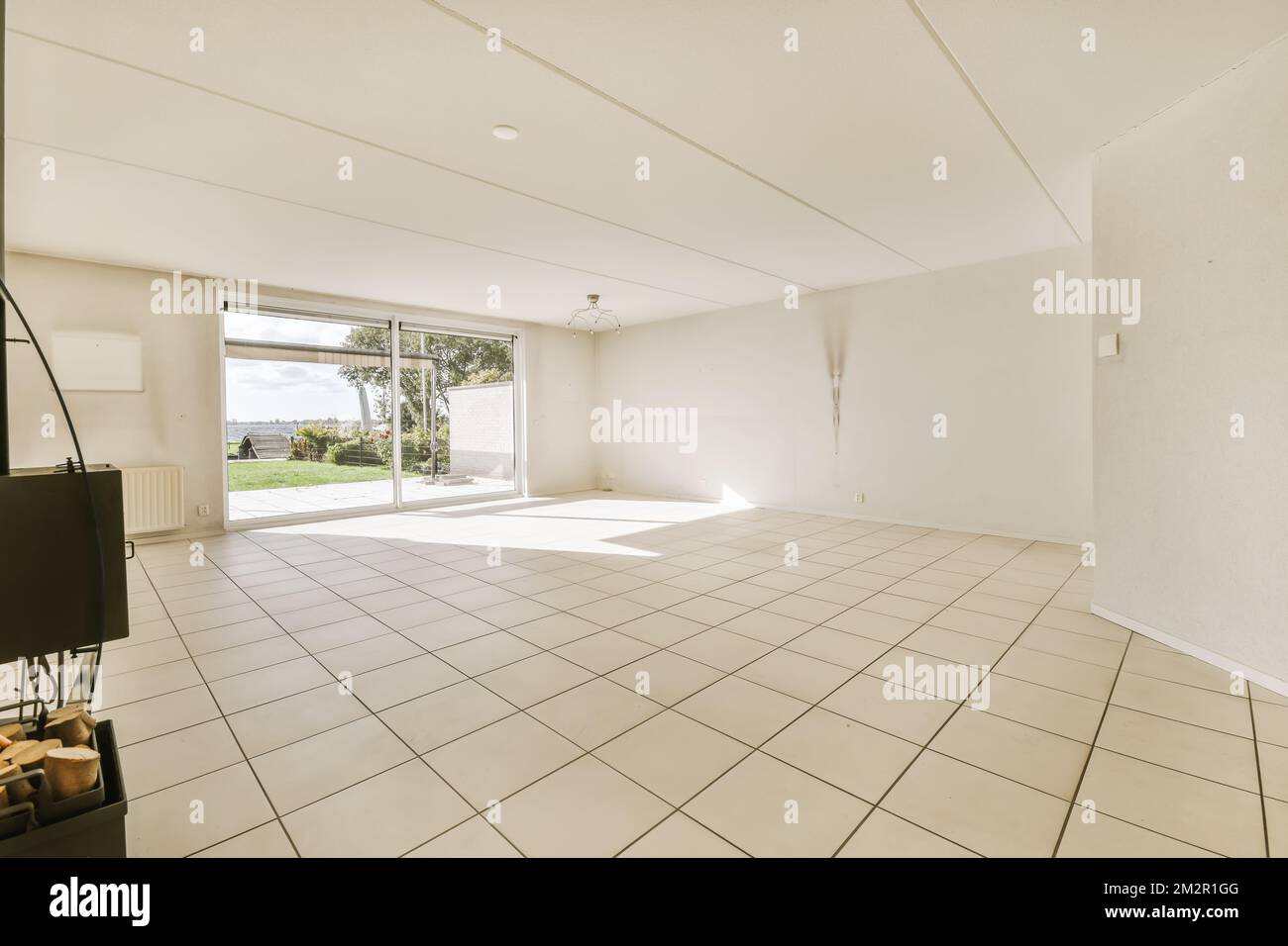 an empty living room with white tile flooring and large sliding glass door leading out to the outside patio area Stock Photo