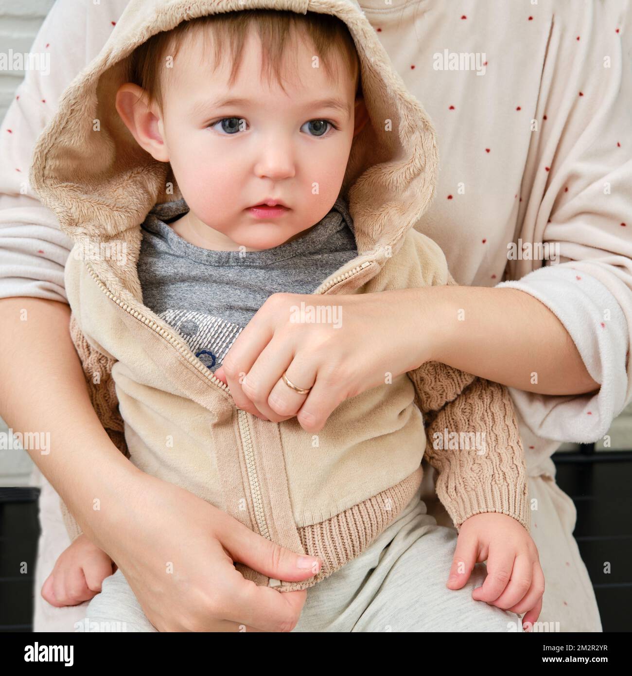 A mother puts a hoodie jacket on a toddler baby sitting in the