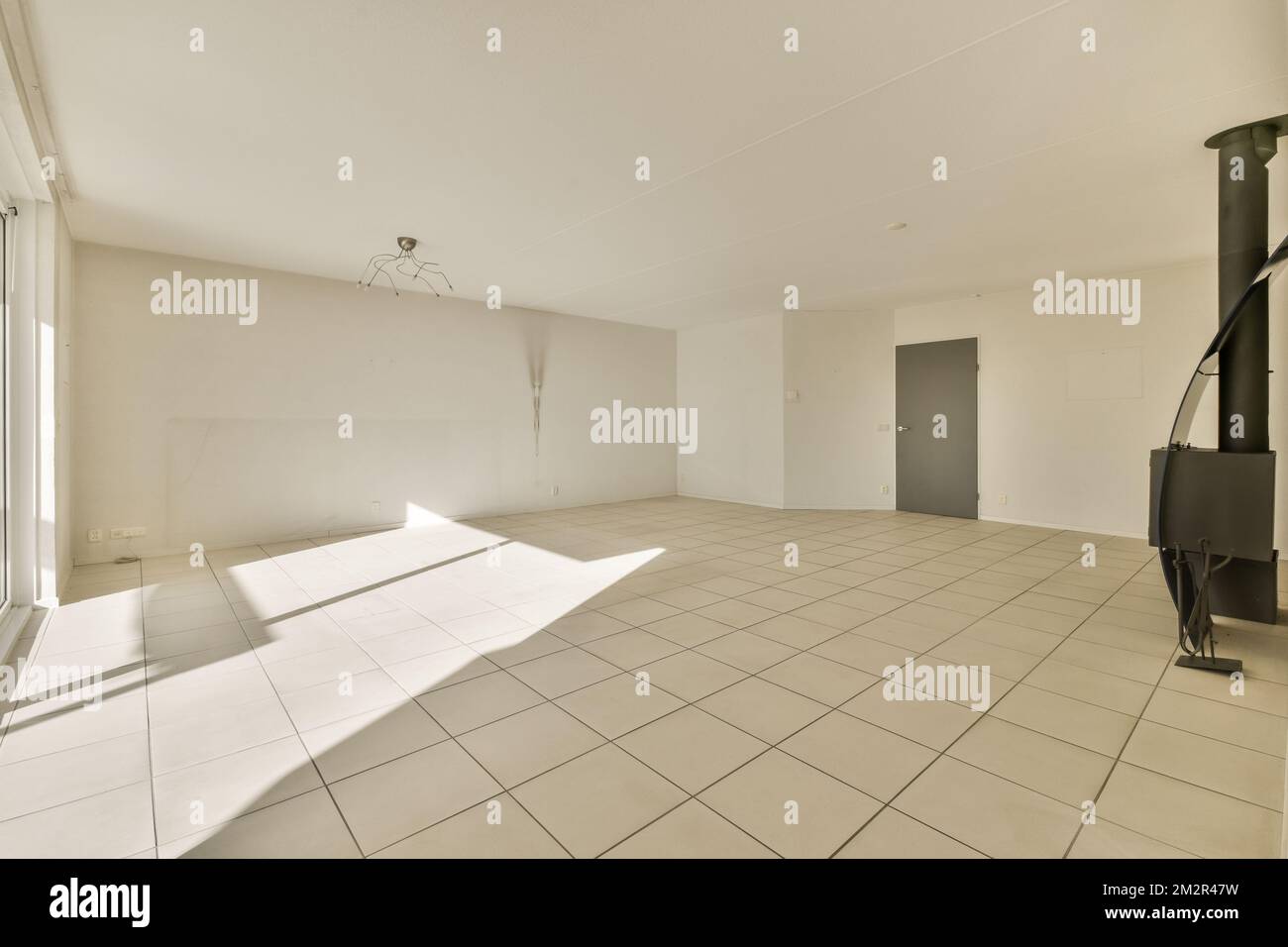 an empty room with white tile flooring and light coming in through the window to see what is going on Stock Photo