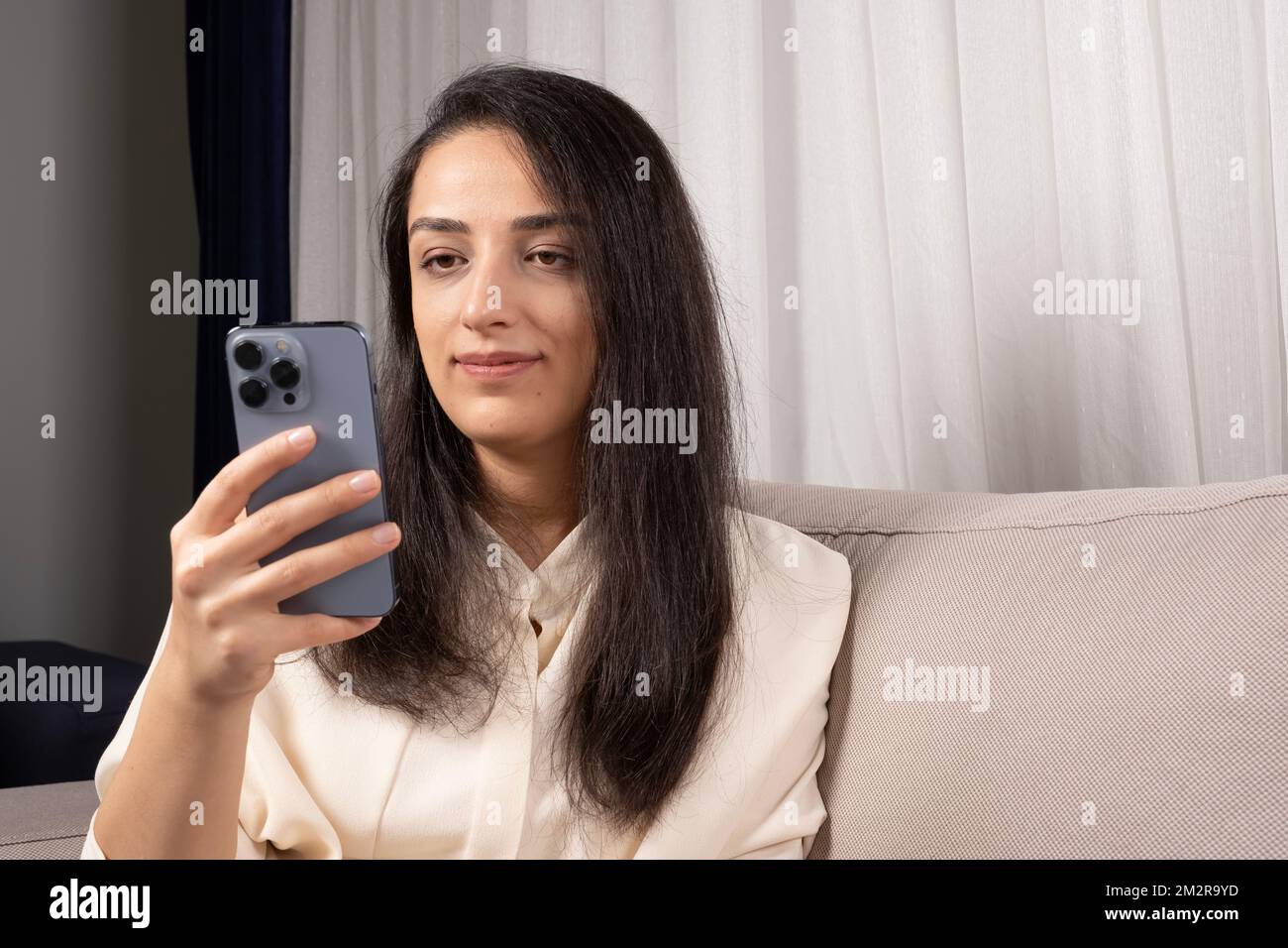 Beautiful caucasian brown haired woman using modern smartphone, cellphone. Sitting at home living room, addiction communication on web, social media. Stock Photo