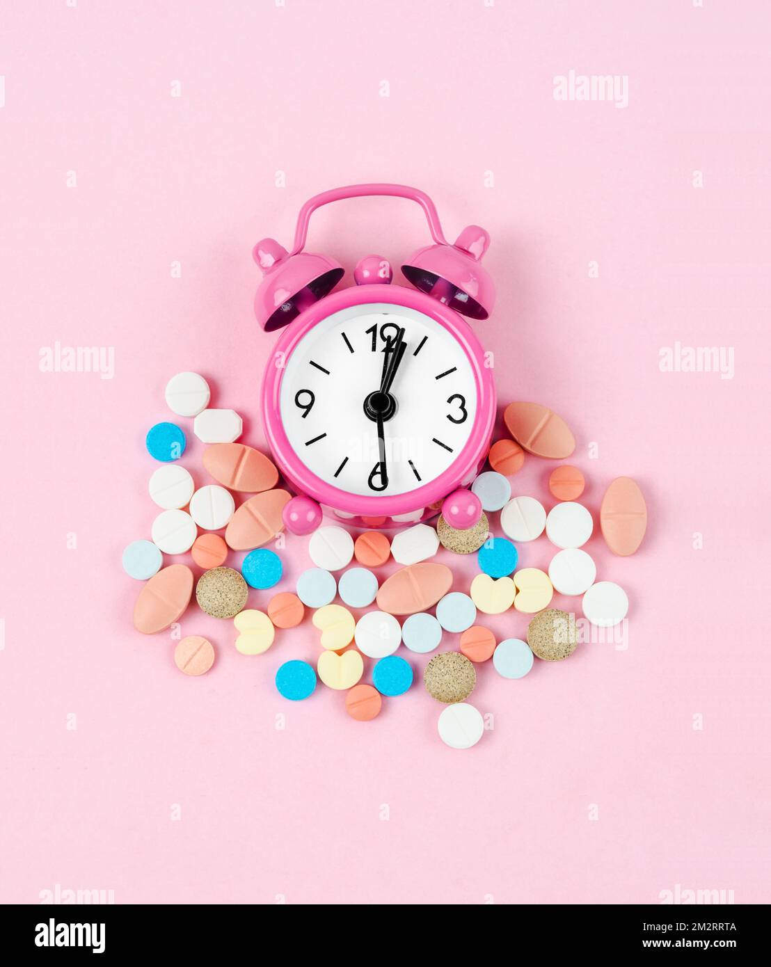 Alarm clock and many drug on a pink colour background. Taking medicine