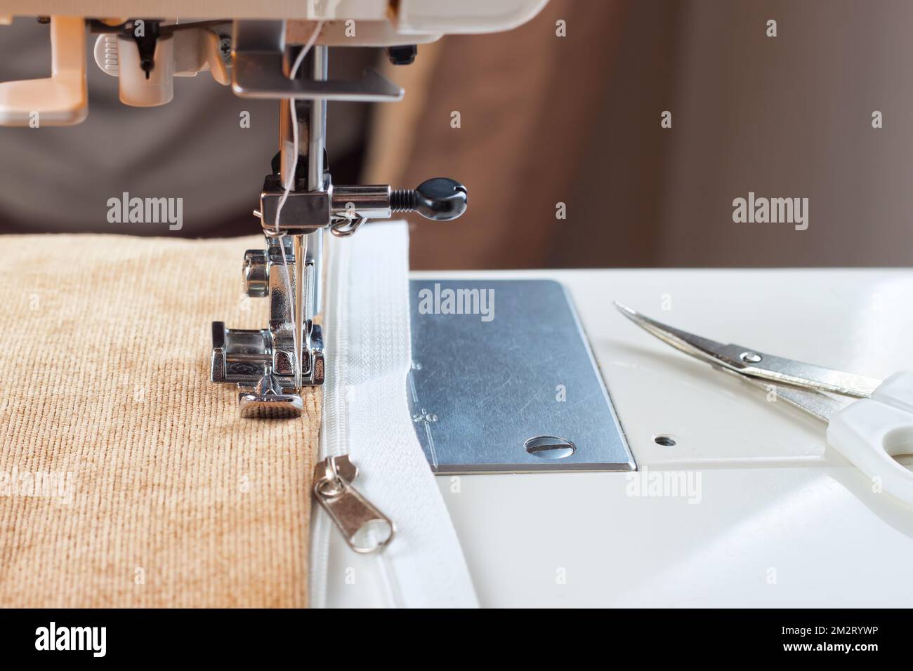 Modern sewing machine sews on the zipper on biege item of clothing