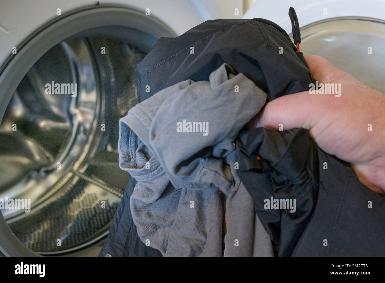 Man's hand folds clothes into an open washing machine. Washing dark