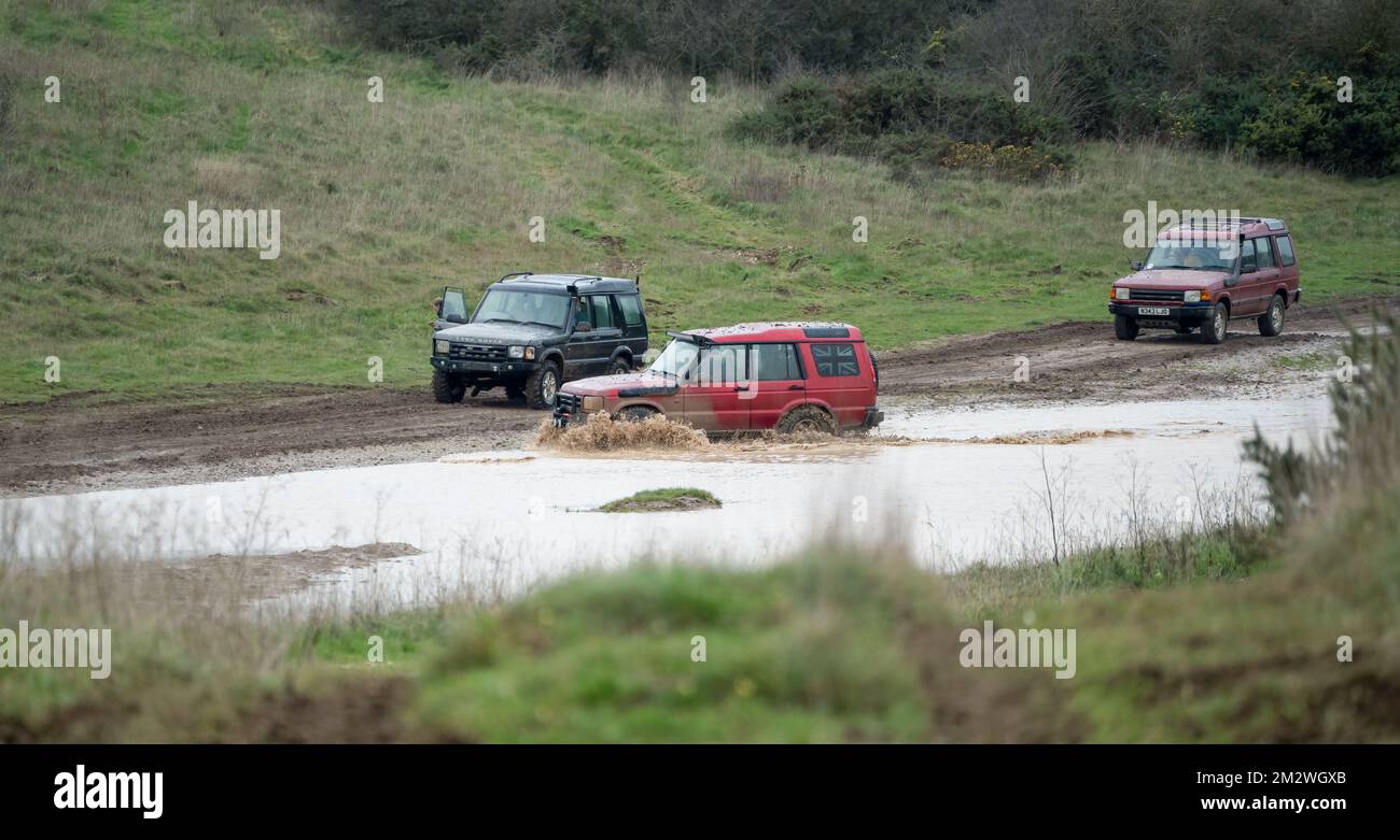 three land rover discovery 4x4 off-road vehicles being driven through deep water and mud in open countryside, Wiltshire UK Stock Photo