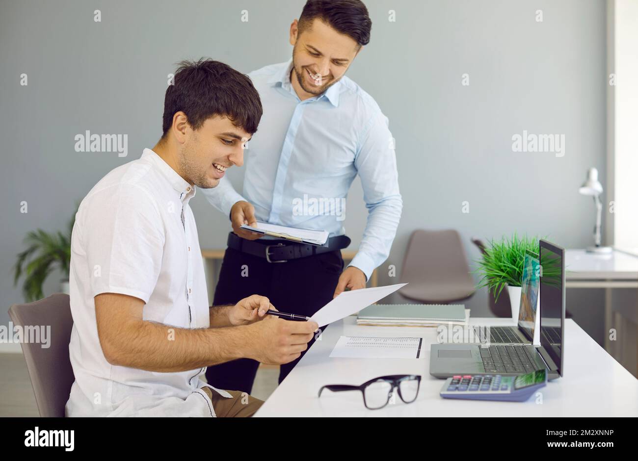 Cheerful colleagues are reviewing and discussing paper documents while working in office. Stock Photo