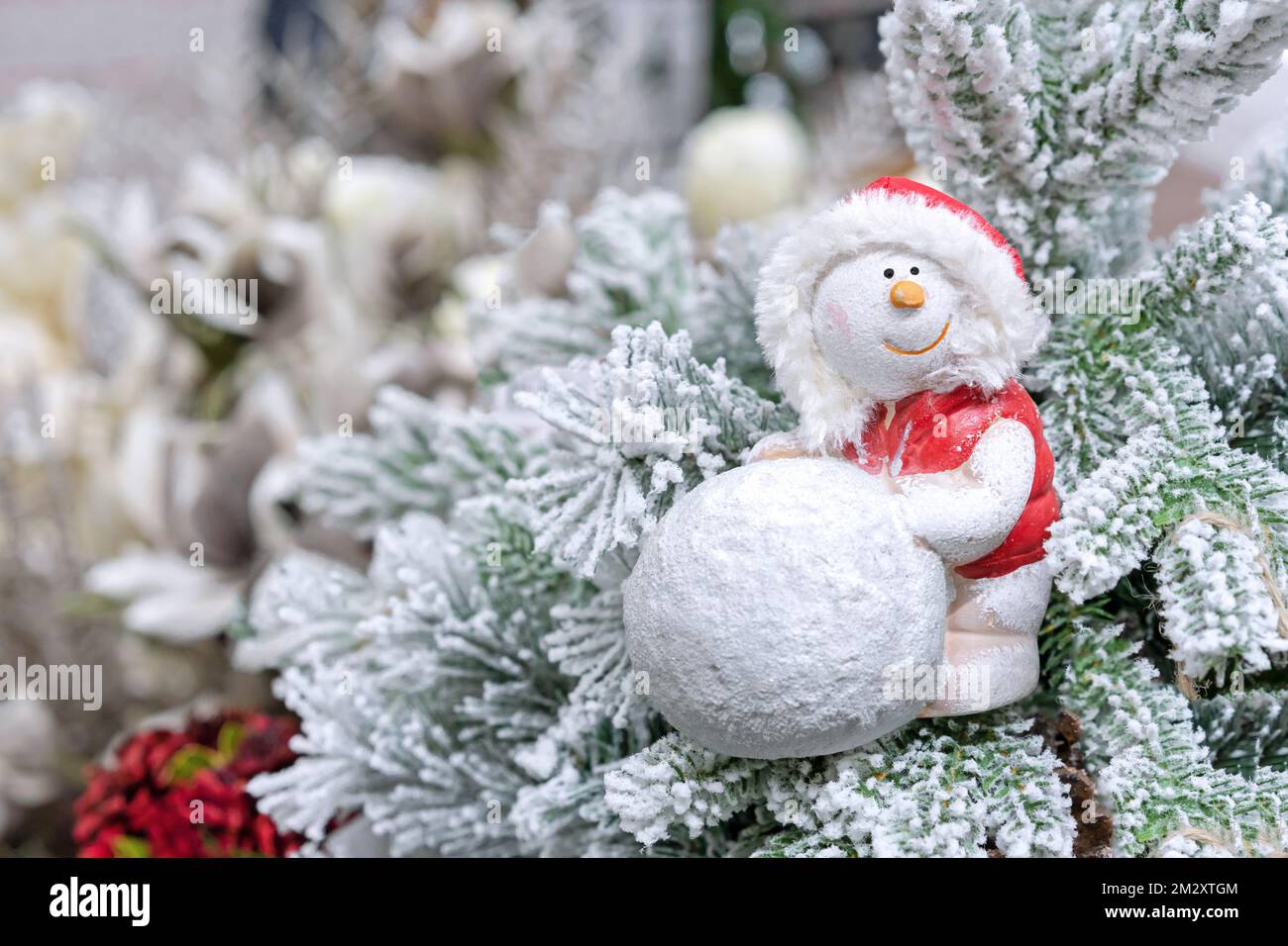 Snowman in a red jacket with a hood and a big snowball on the snow-covered christmas tree. Stock Photo