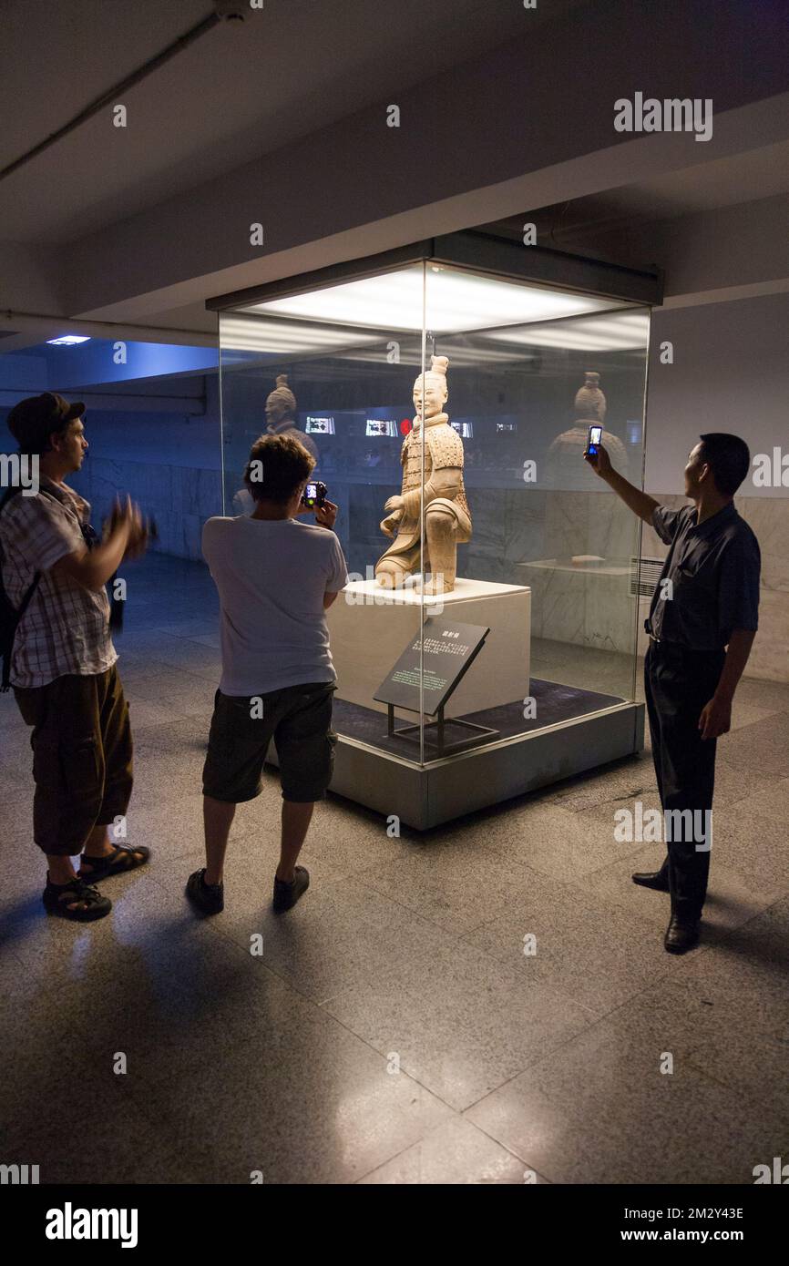 Chinese tourists view and take photographs on their mobile phone device of the kneeling archer figure, made from terracotta clay, excavated from Pit 2 and now on display to tourist in that building. The Terracotta Army at Emperor Qinshihuang's Mausoleum Site Museum in Xi'An. PRC. China. (125) Stock Photo