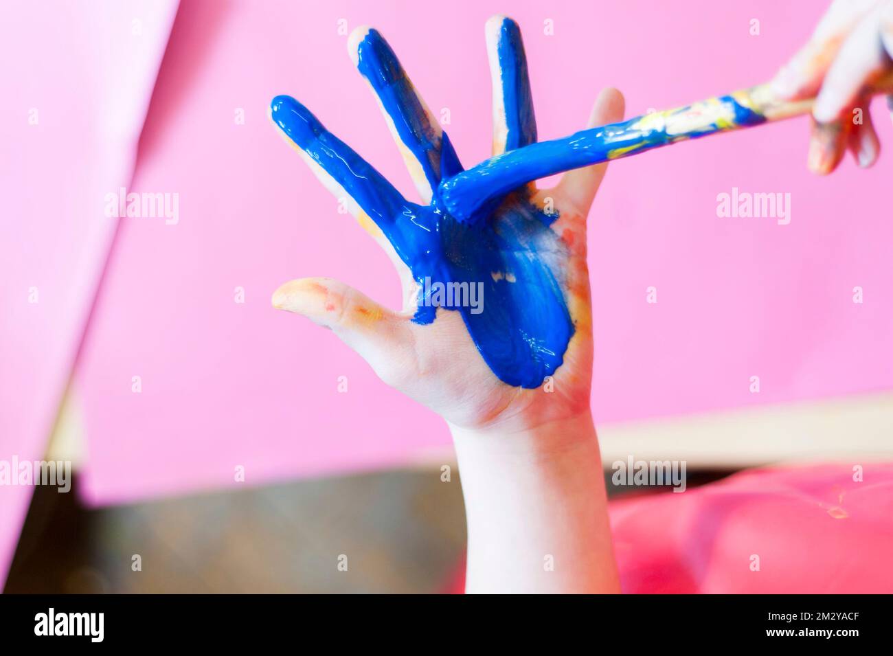 Close up of child using paint brush to paint their hand with blue paint
