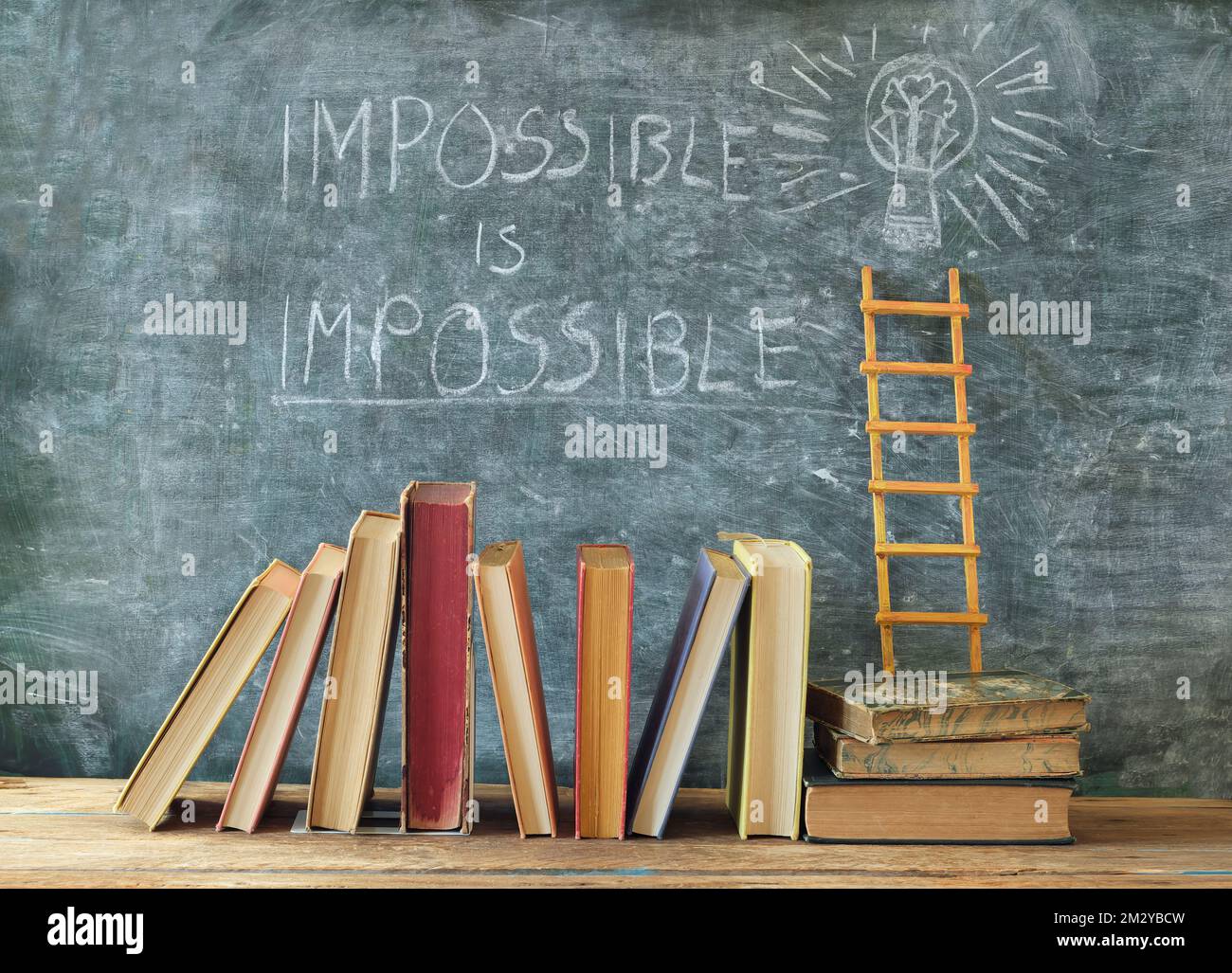 Stack of hardback books with slogan impossible is impossible on blackboard.Learning,education,development, ladder of sucess and back to school concept Stock Photo