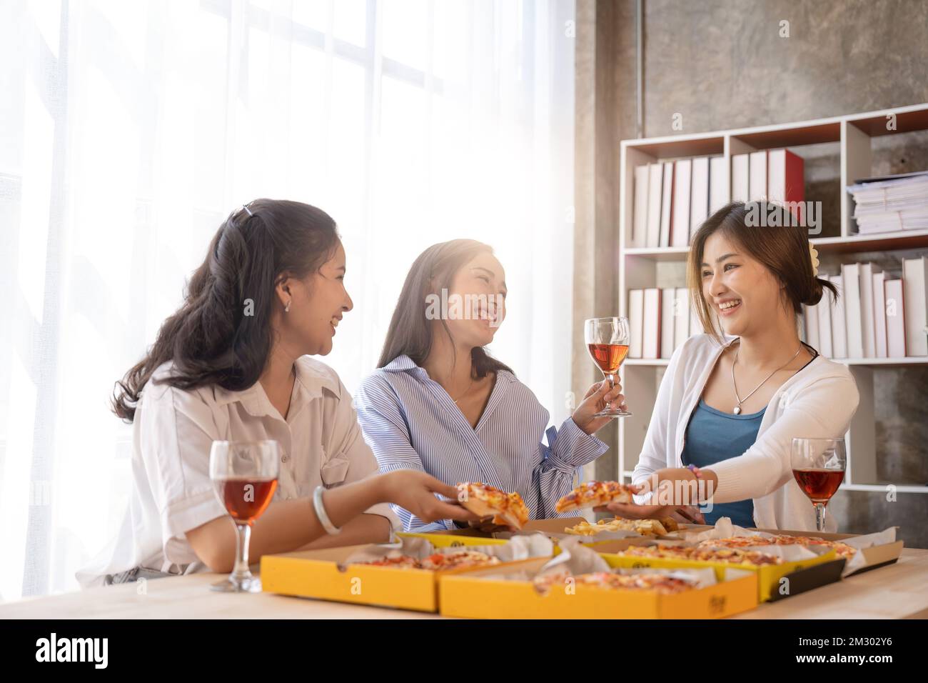 Group of Asian friends gather to celebrate Christmas with champagne and eating pizza at home. Joy of holiday party with friends or colleague concept Stock Photo