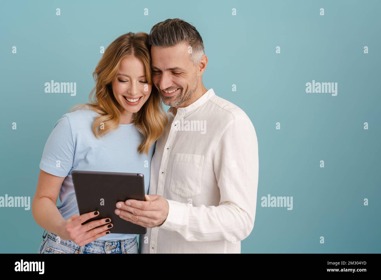 White happy couple hugging and using tablet computer isolated over blue background Stock Photo