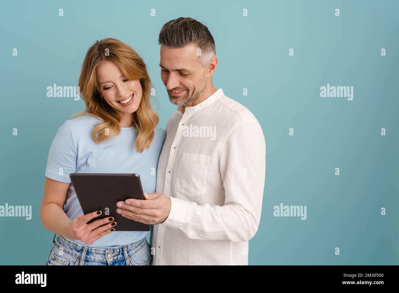 White happy couple hugging and using tablet computer isolated over blue background Stock Photo
