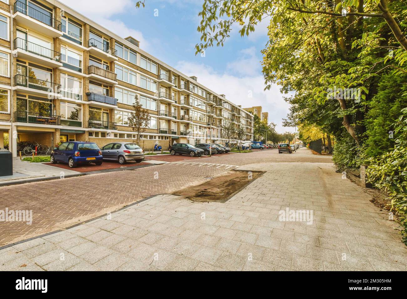 an apartment complex with cars parked on the street and trees lining ...
