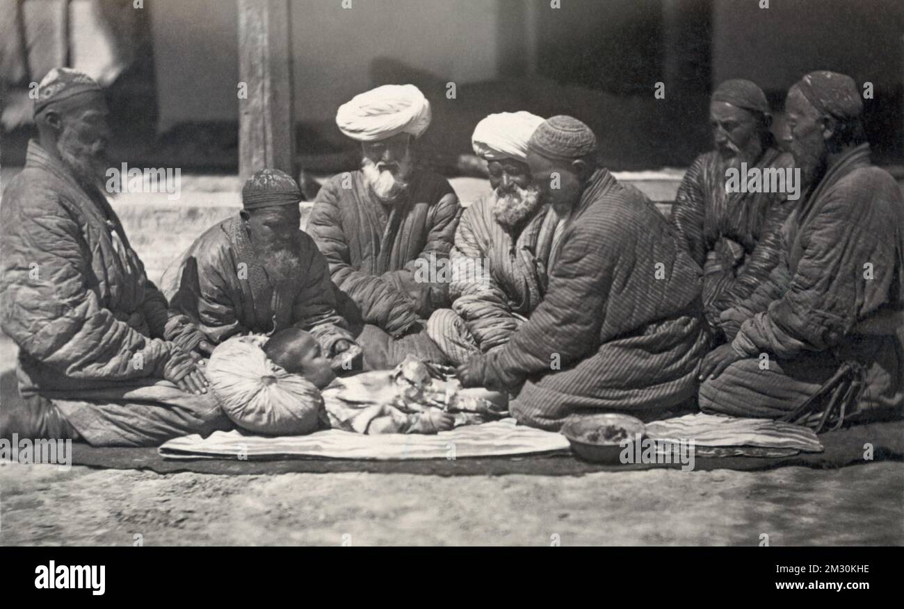 Circumcision - Central Asia - 1865-1872 - Photograph shows a group of men seated on the ground near a small boy who is being circumcised. Stock Photo
