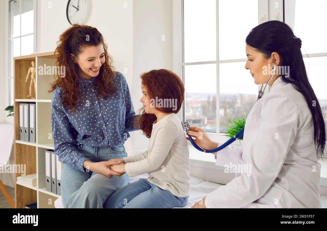 Joyful woman with daughter visits doctor pediatrician and holds child hand sits in hospital Stock Photo