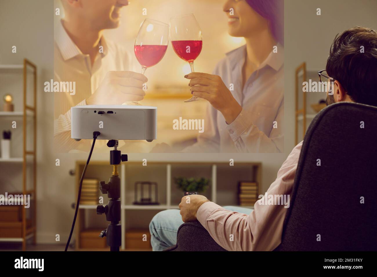 Lonely man is relaxing at home in evening watching romantic movie on TV projector. Stock Photo