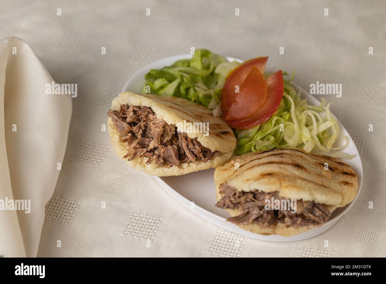Arepas, typical Venezuelan food, made with maize and filled with shredded meat on white tablecloth. Stock Photo