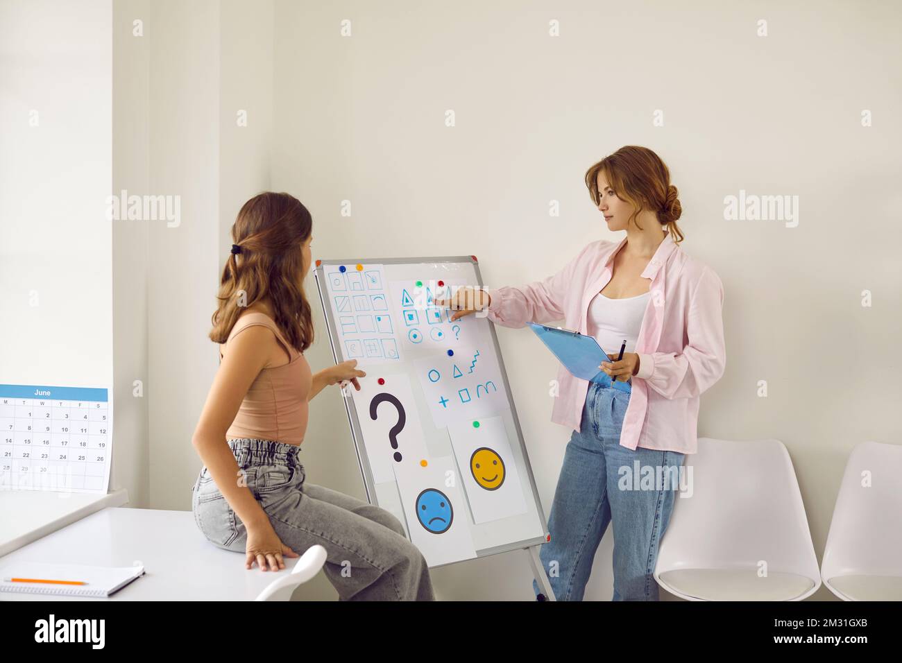 Professional female psychologist tells teenage girl more about psychology using white board. Stock Photo
