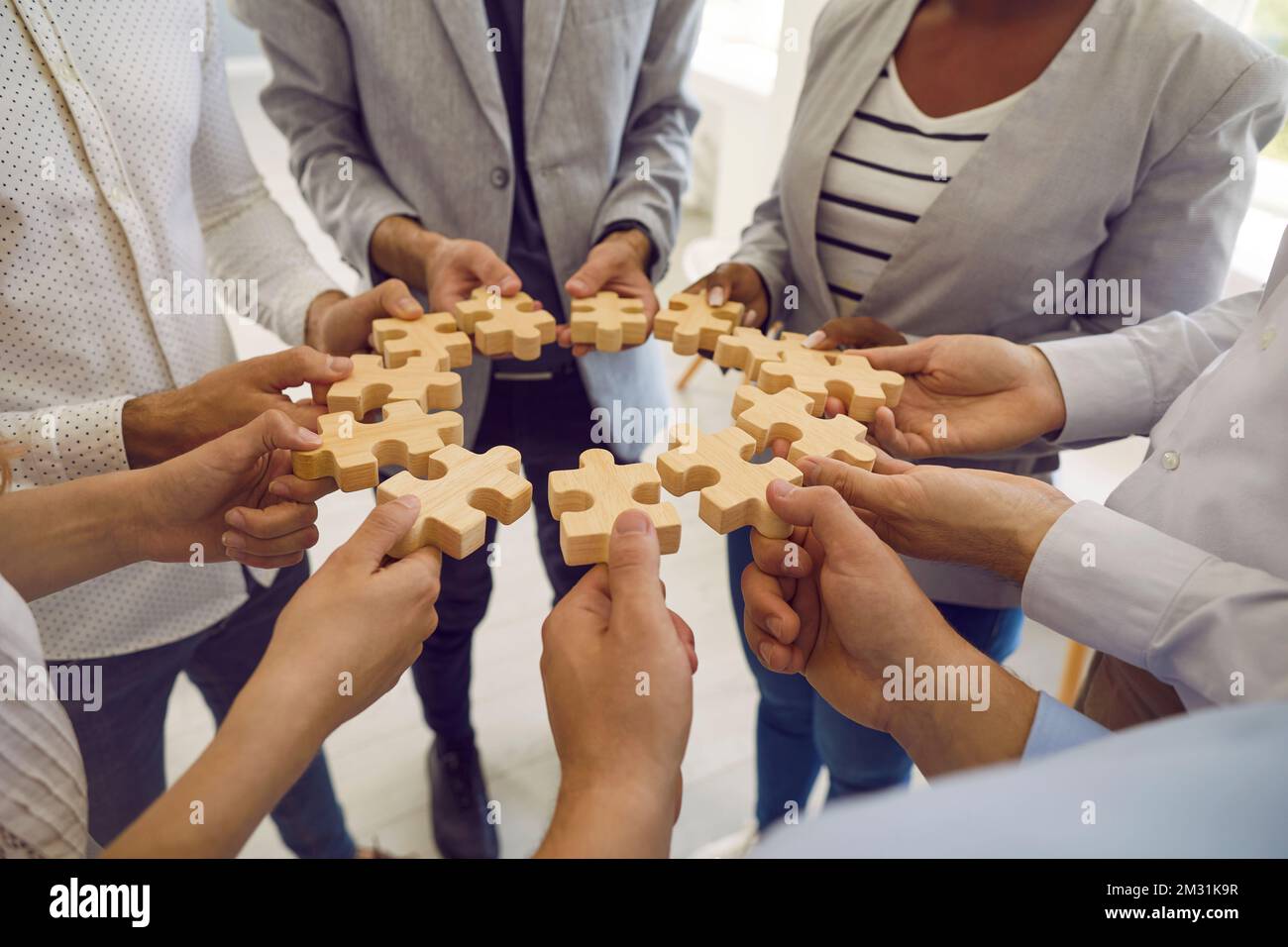 Group of men and women standing in circle and connecting identical wooden puzzle pieces. Stock Photo