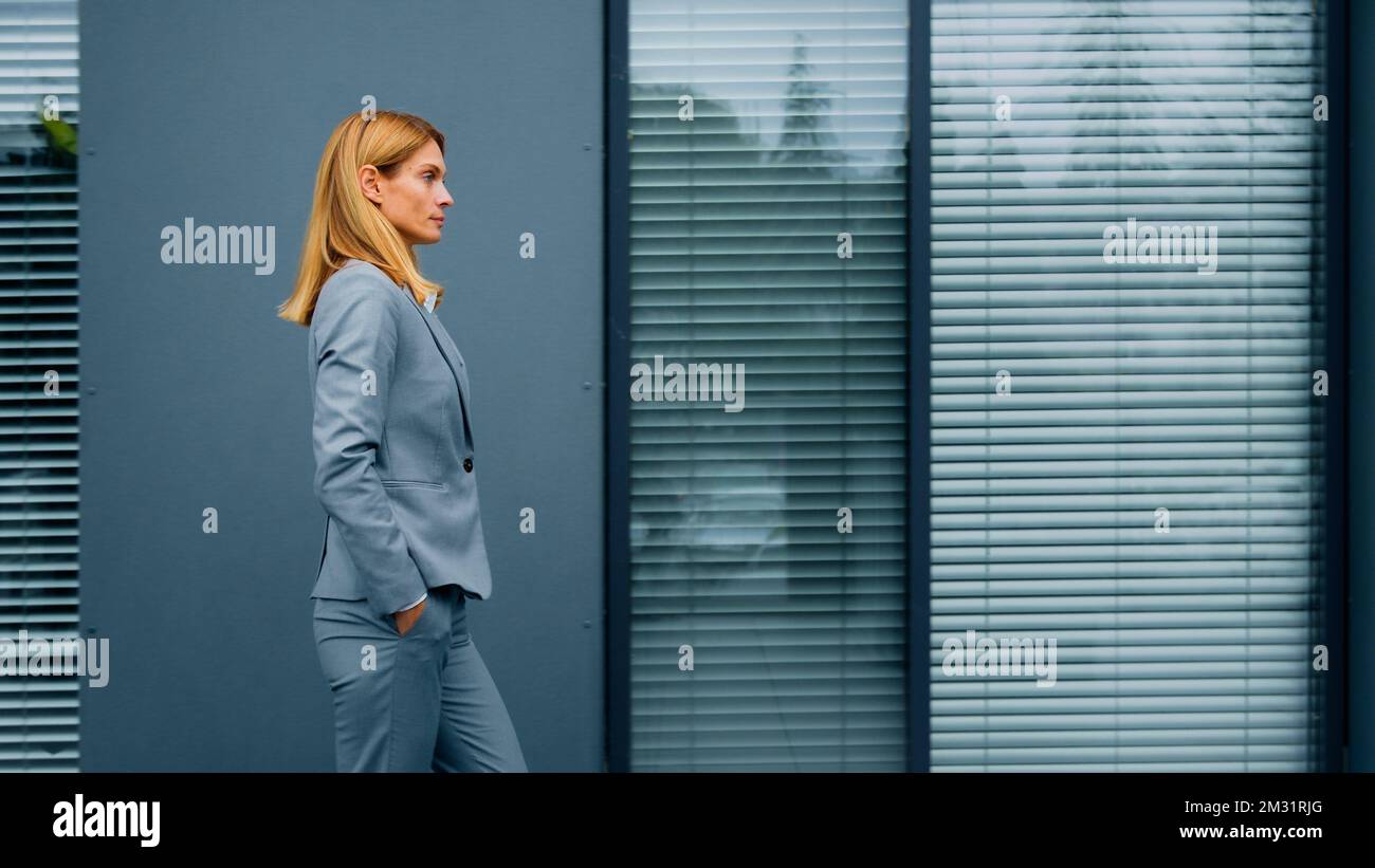 Proud confident stylish woman leader boss professional worker in formal suit walking down street against backdrop of office building successful Stock Photo