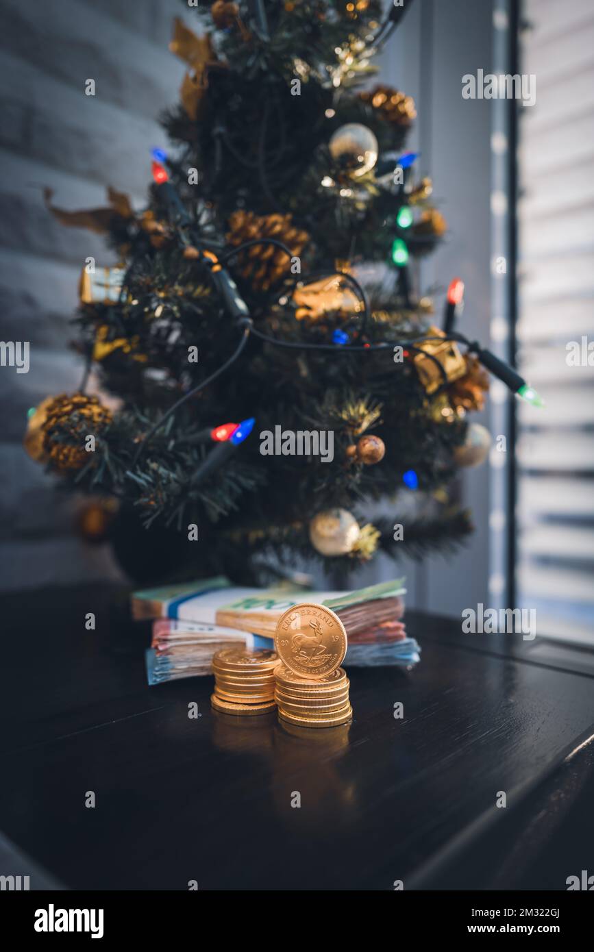 under a christmas tree lies a bundle of cash and a stack of Krugerrand gold coins Stock Photo