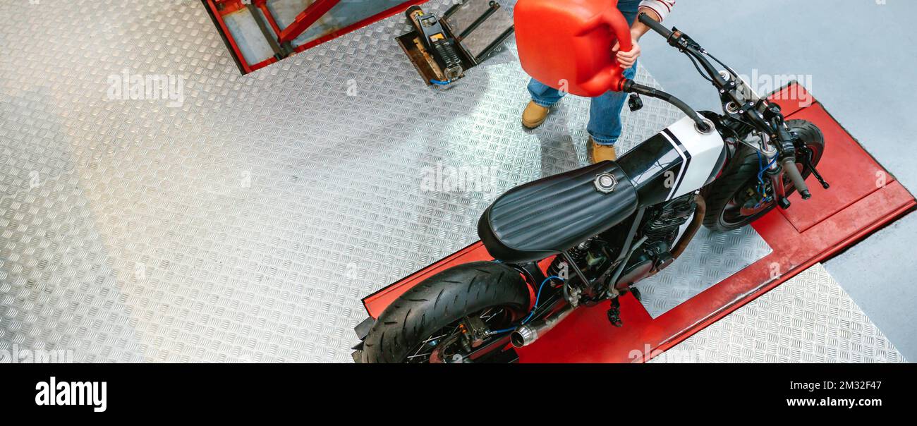 Mechanic woman with jerry can filling fuel tank of motorcycle on
