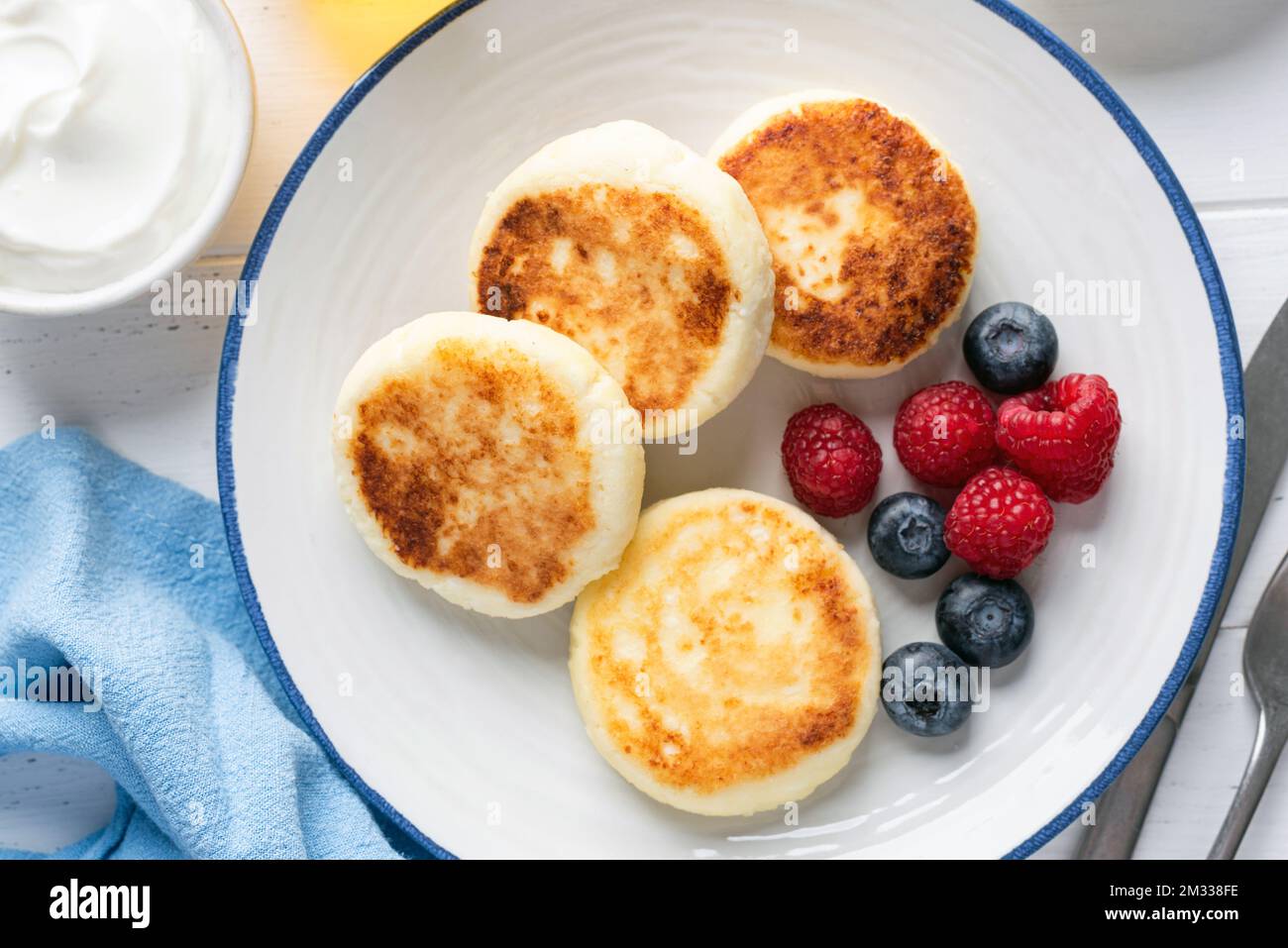 Sweet breakfast cheese pancakes or fritters Syrniki served with berries on white plate, top view Stock Photo