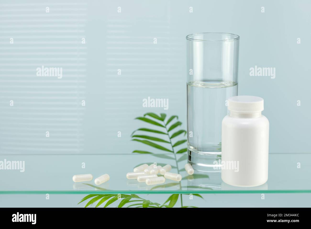 Health care composition with pills and glass of pure water on glass shelf with palm leaves and copy space. Flu season and no virus concept. Mock up of Stock Photo