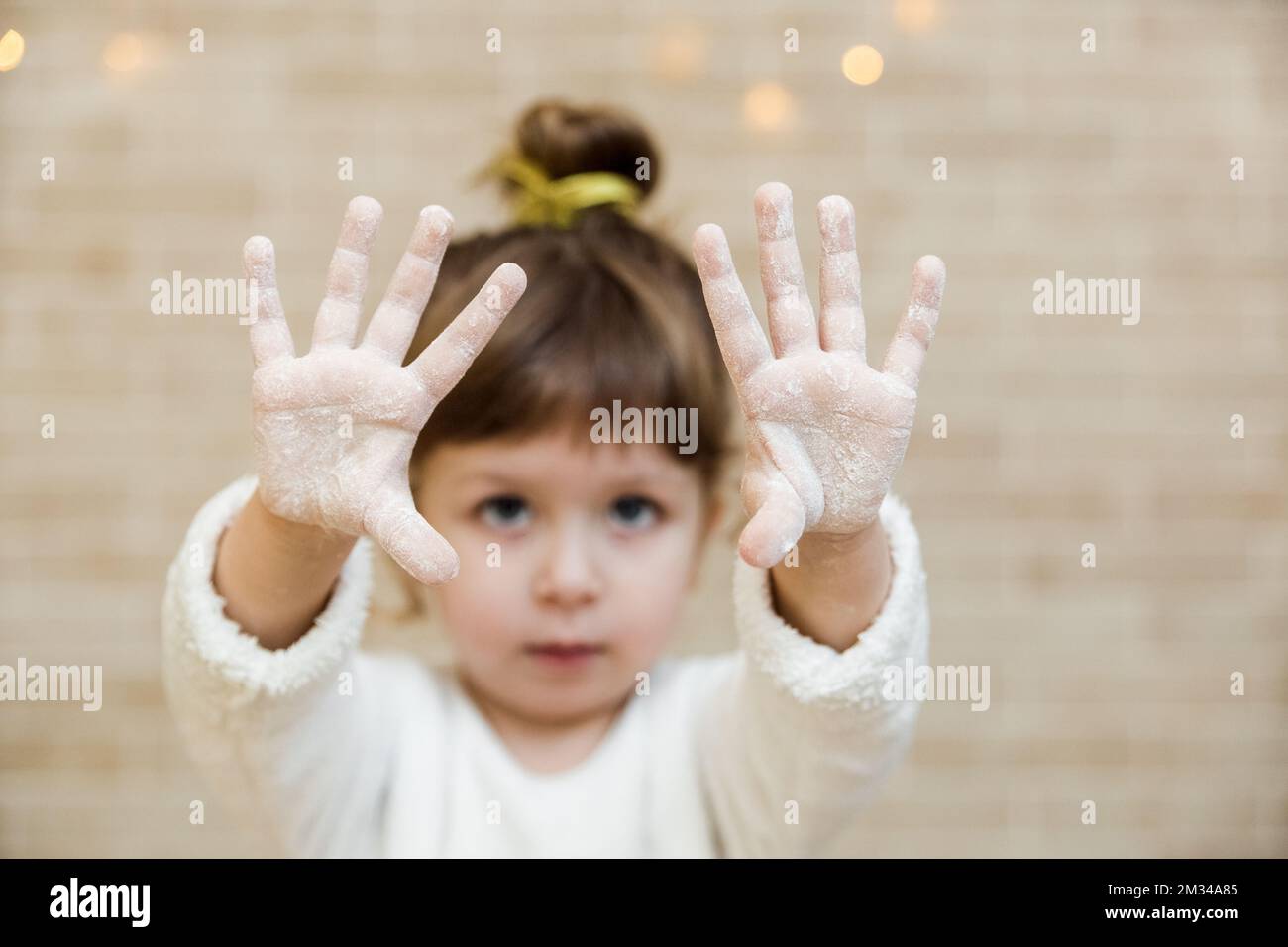 Brunette baby girl is preparing gingerbread in Christmas kitchen. Funny little girl is covered in flour.Children chef concept. Stock Photo