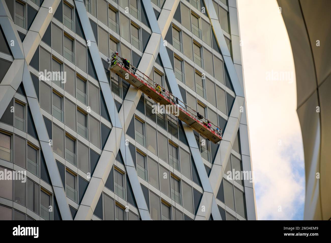 LONDON - November 4, 2020: Men work from suspended platform on side of skyscraper in London Docklands Stock Photo