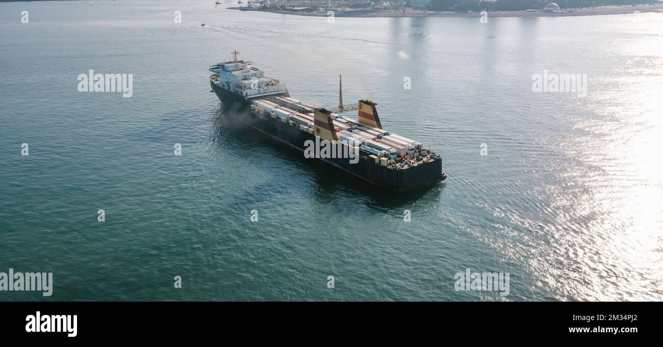 Cargo freight ship with containers and trucks sailing to industrial logistic port, aerial view from drone. Stock Photo