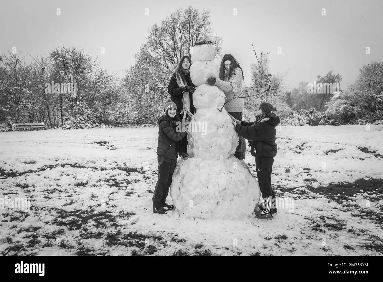 Black and white image of 4 teenagers in Hampstead posing proudly by their giant snowman which took them two hours to build. Stock Photo