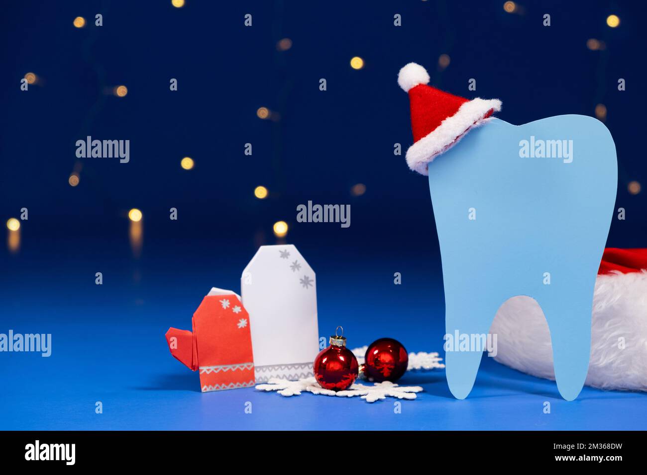 Christmas dentistry - tooth with red santa claus hat, mittens on a blue background. Stock Photo