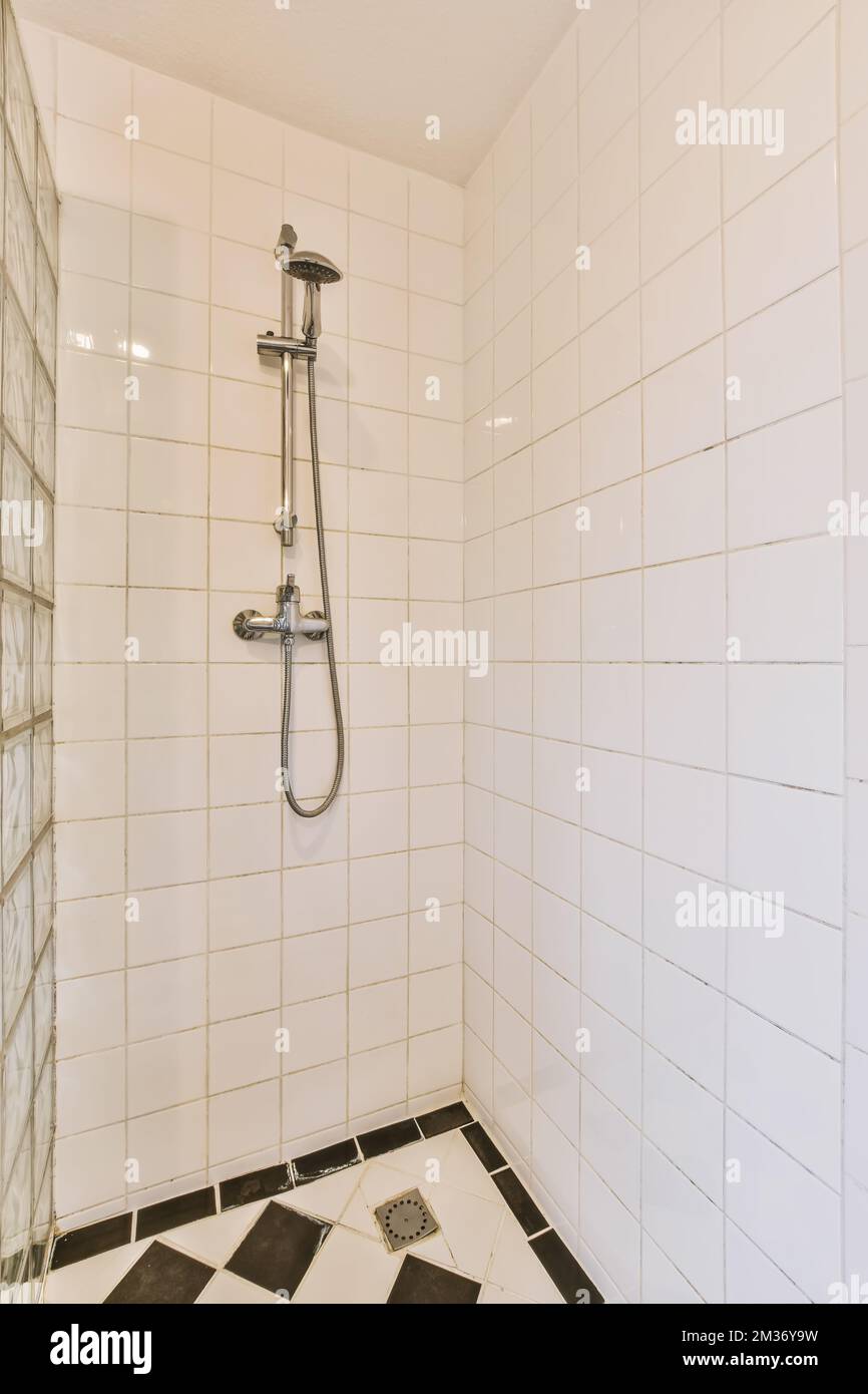 https://c8.alamy.com/comp/2M36Y9W/a-bathroom-with-black-and-white-tiles-on-the-floor-shower-head-is-in-the-center-of-the-tileed-wall-2M36Y9W.jpg
