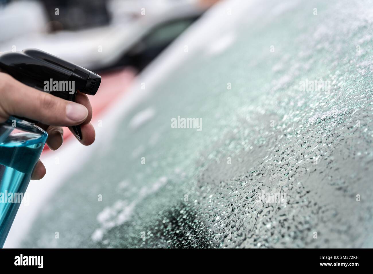 Man uses a bottle of de-icer to defrost the ice-covered windshield Stock Photo