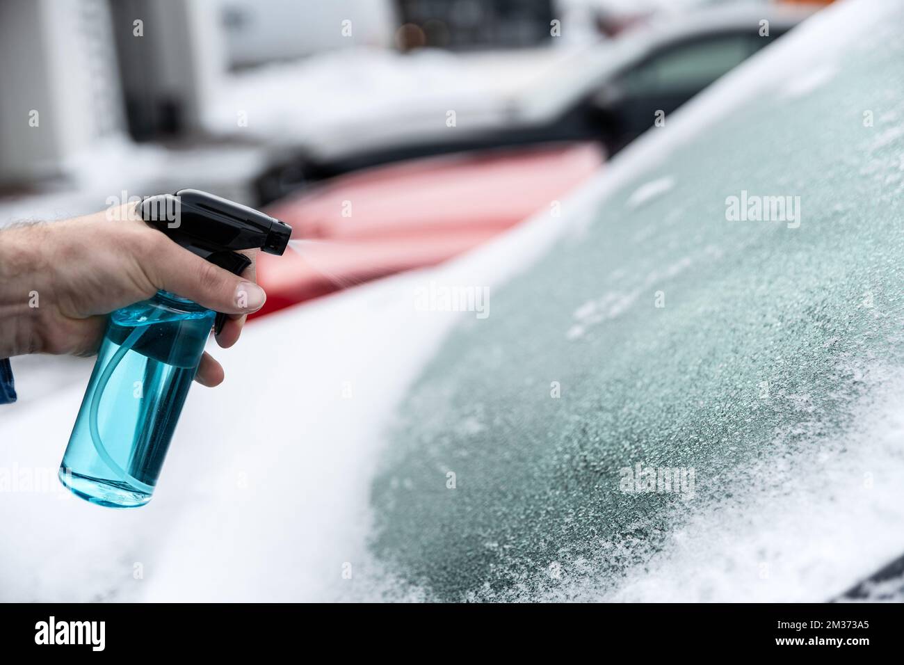 Man uses a bottle of de-icer to defrost the ice-covered windshield Stock Photo