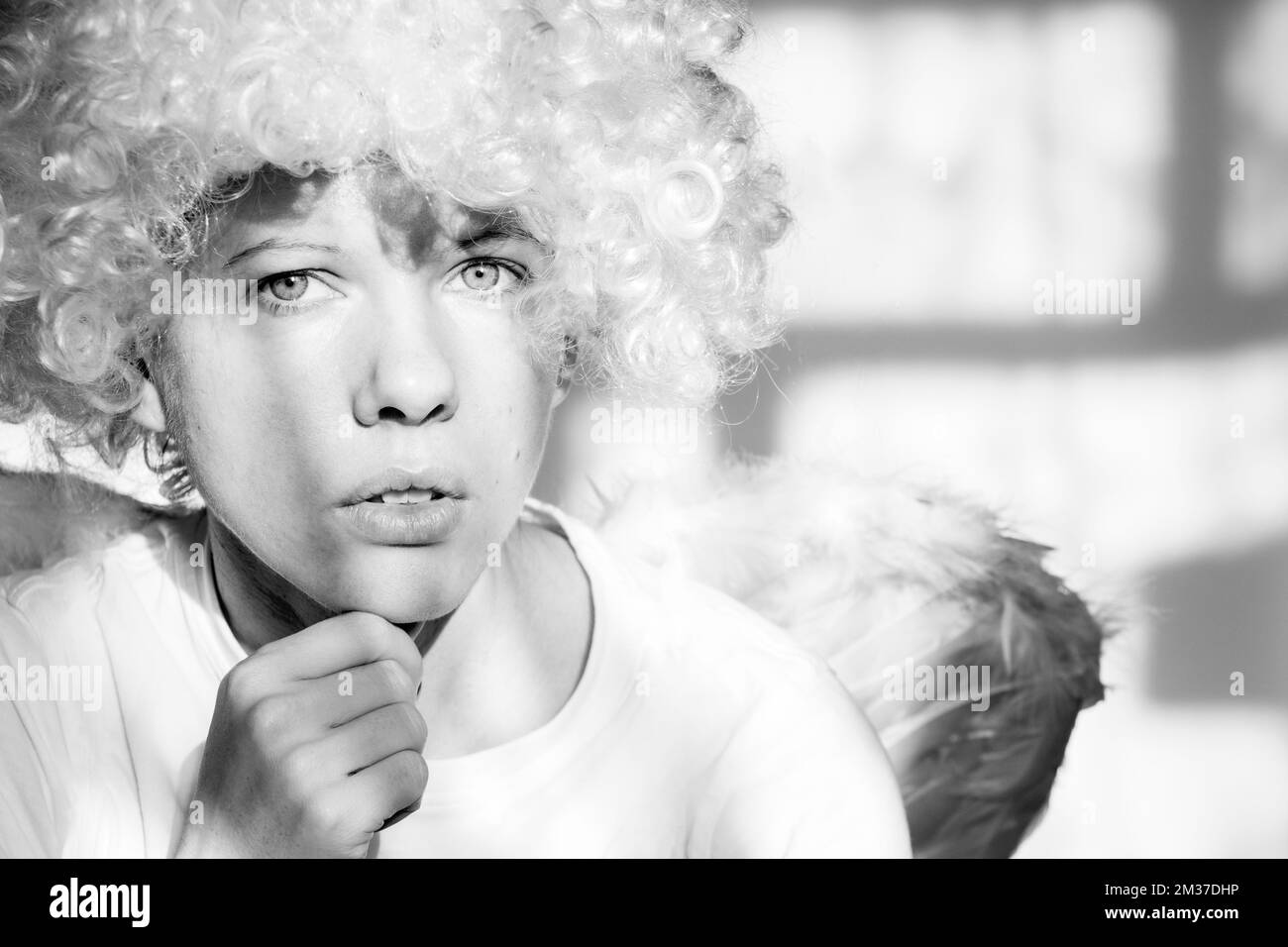 Girl in an angel costume with wings and curly hair on an isolated background with shadows on the wall Stock Photo