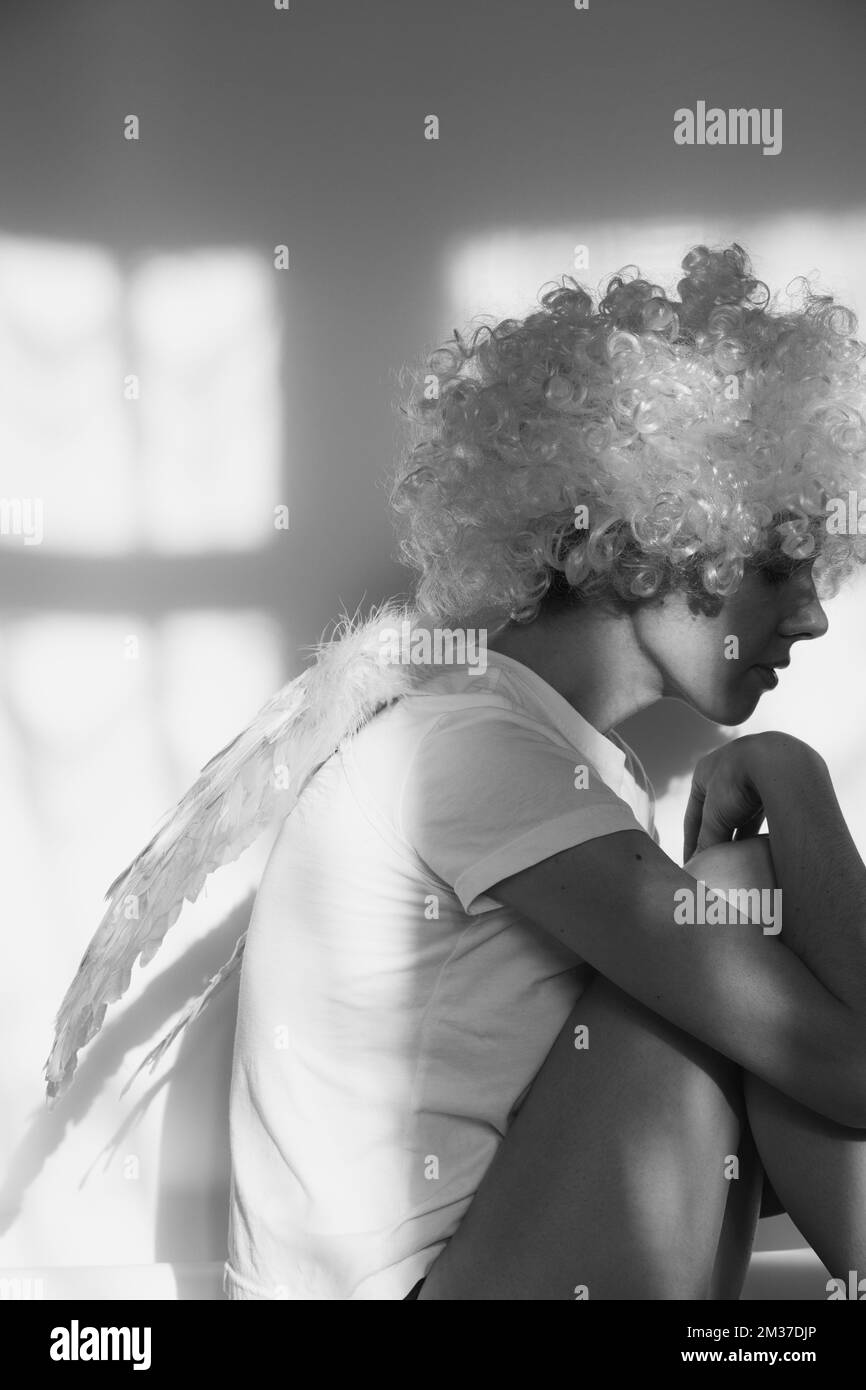 Girl in an angel costume with wings and curly hair on an isolated background with shadows on the wall Stock Photo