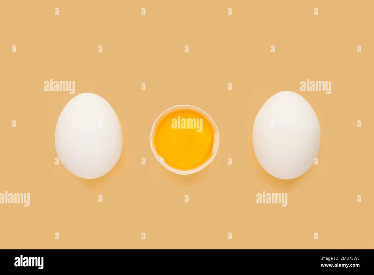 Whole chicken Eggs and cracked half with yolk on yellow background. Minimalism Stock Photo