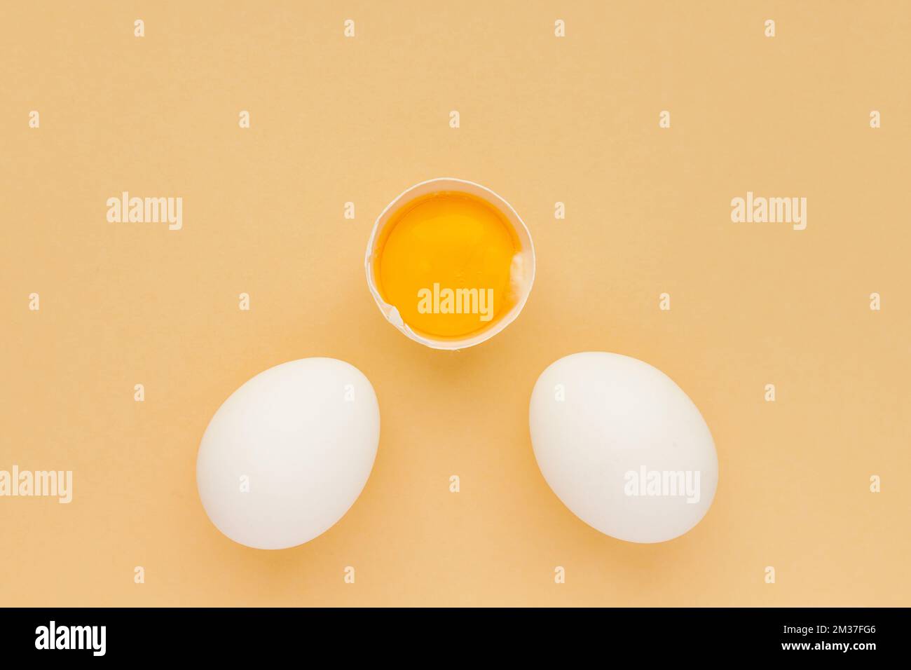 Whole white chicken Eggs and cracked half in the middle with raw yolk on yellow background. Minimalism. Top view Stock Photo
