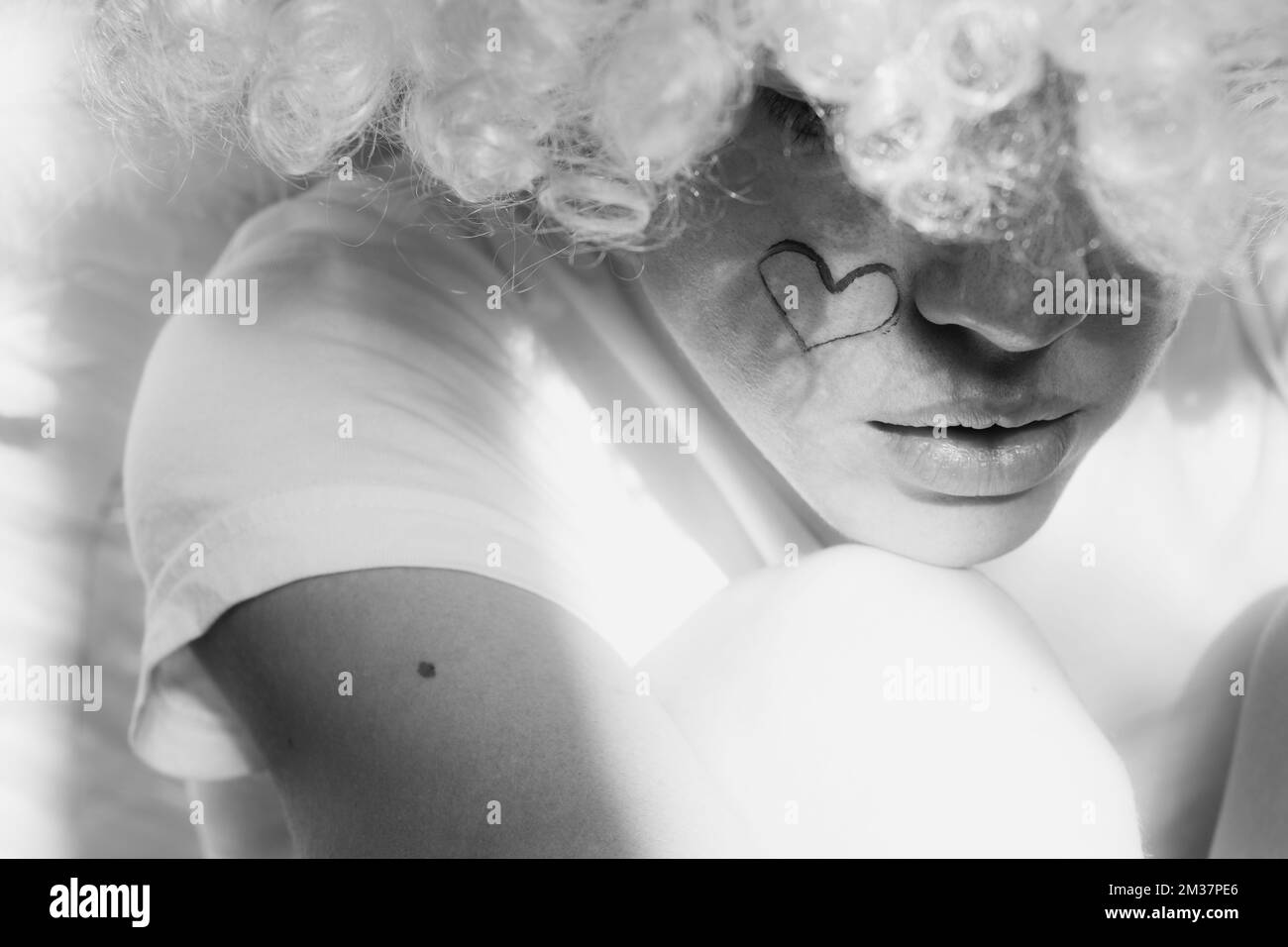 Girl dressed as an angel with wings and curly hair with a painted heart ...