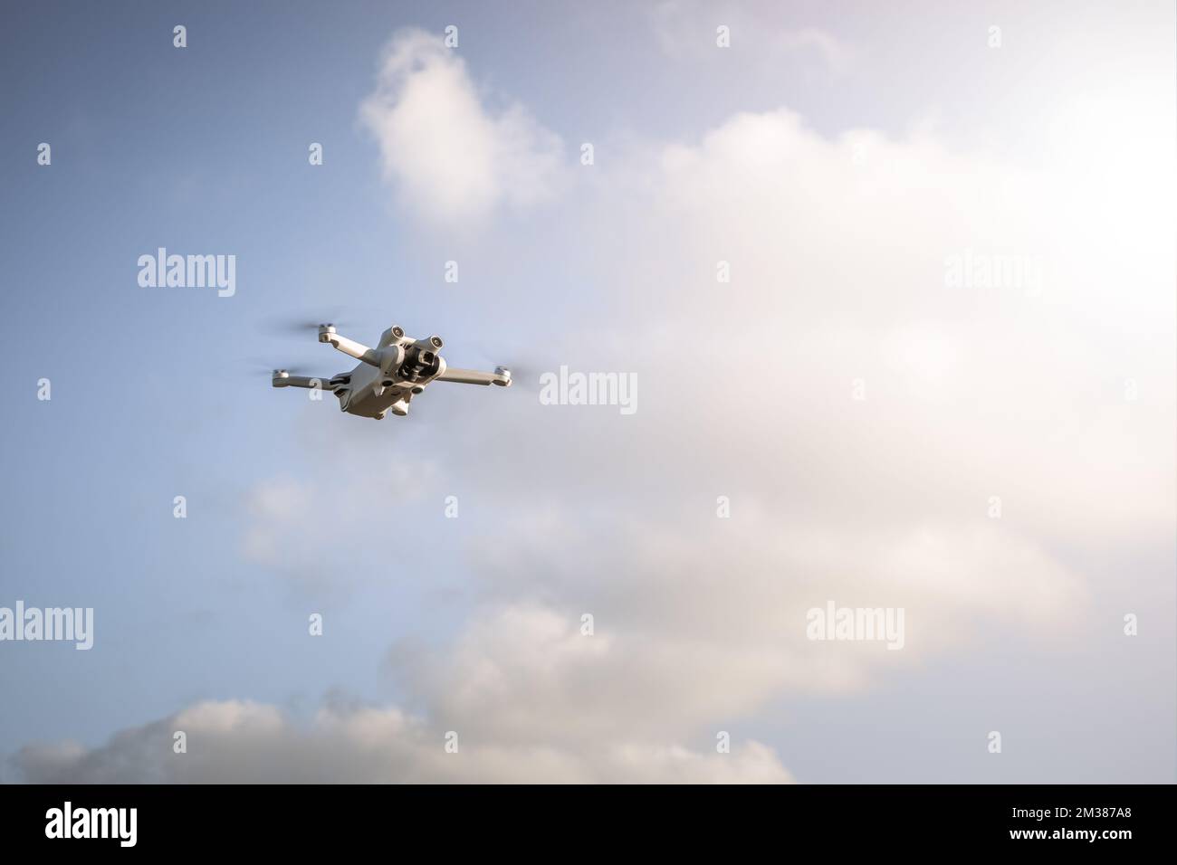 A white quadcopter flying in the sky on a sunny day Stock Photo