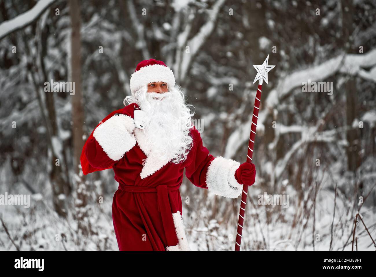 Santa Claus with bag of Christmas gifts is walking in snow forest. Stock Photo