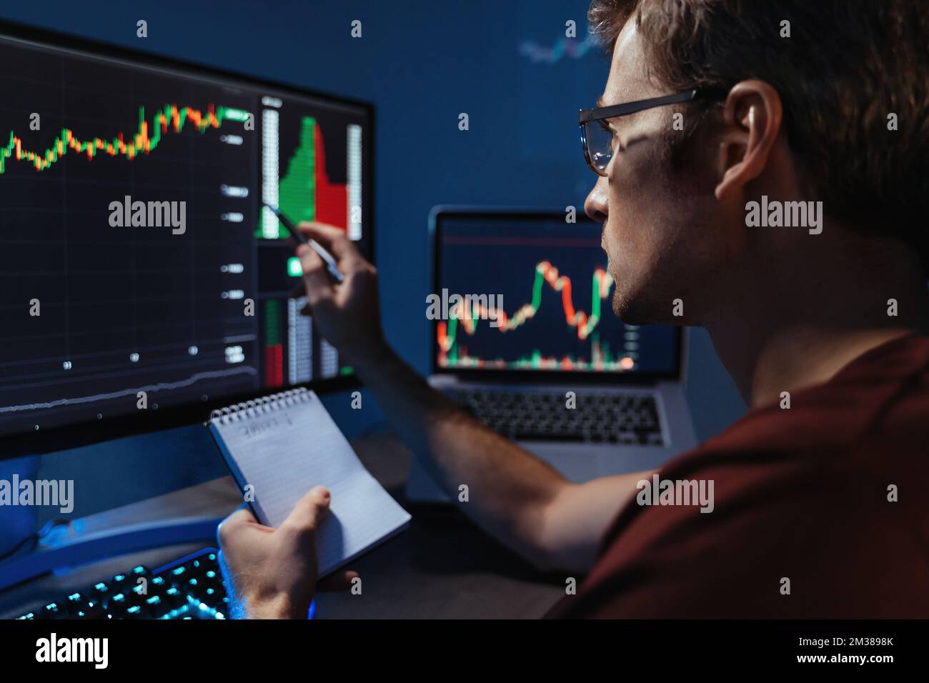 Close up of crypto trader making technical analysis to identify and predict trends and patterns in value changes of cryptocurrency, reading candlestick chart, making notes in notepad Stock Photo