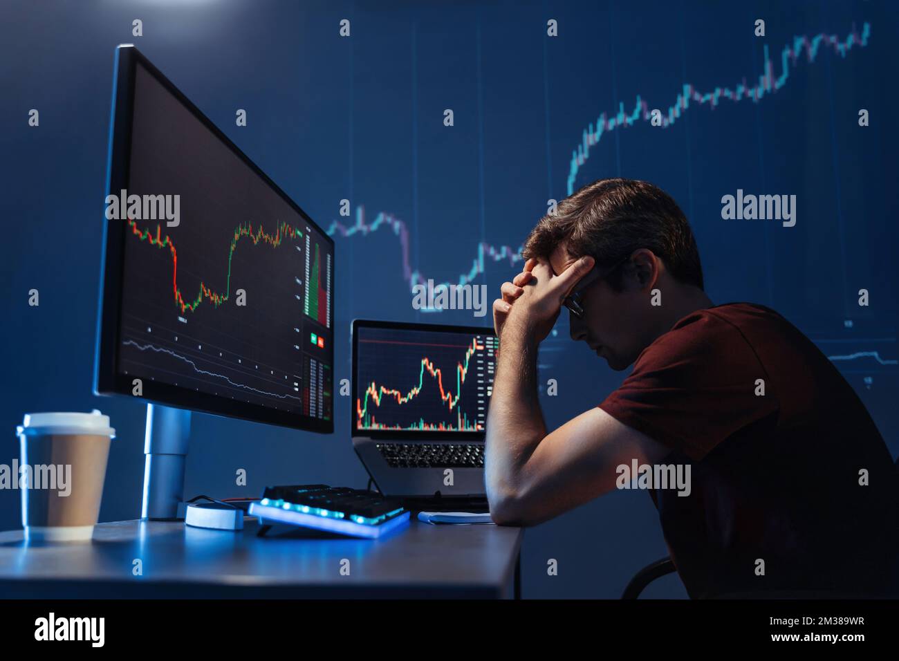 Side view of depressed thoughtful male crypto investor holding head in hands in front of computer with candlestick chart of crypto currency market, failed gaining money, upset with global recession Stock Photo