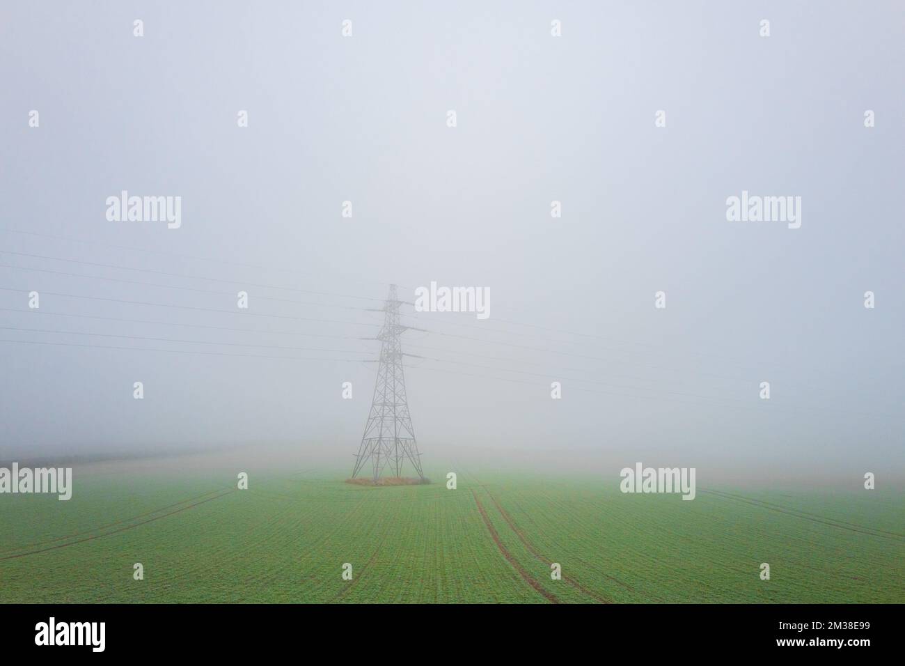 275 KV overhead power line attached to a latice  steel tower in a field on a foggy winters day Stock Photo