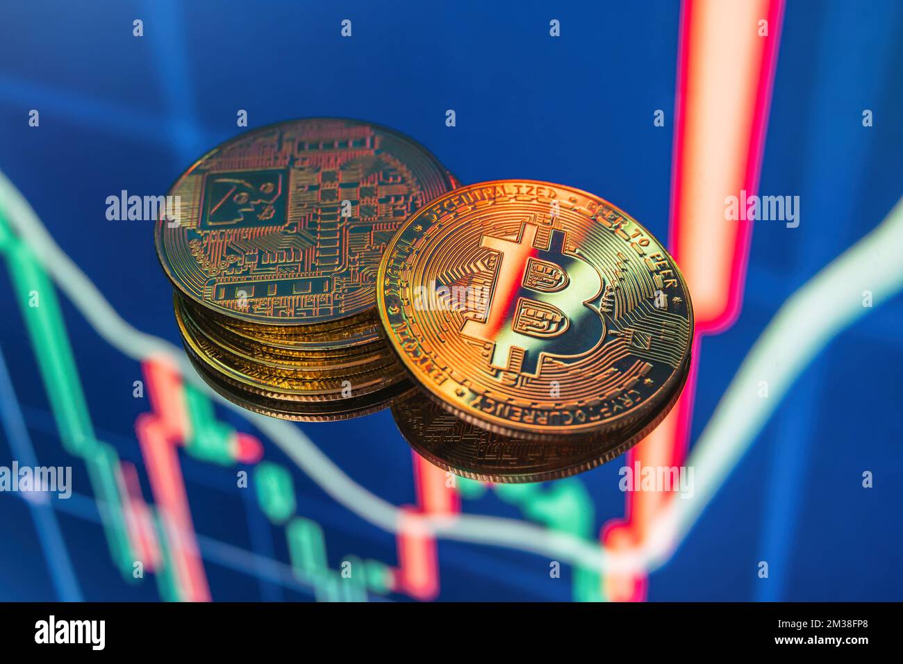 Closeup of stacked golden bitcoin cryptocurrency lying on blue digital display with candle stick graph chart representing investment stock exchange fund Stock Photo