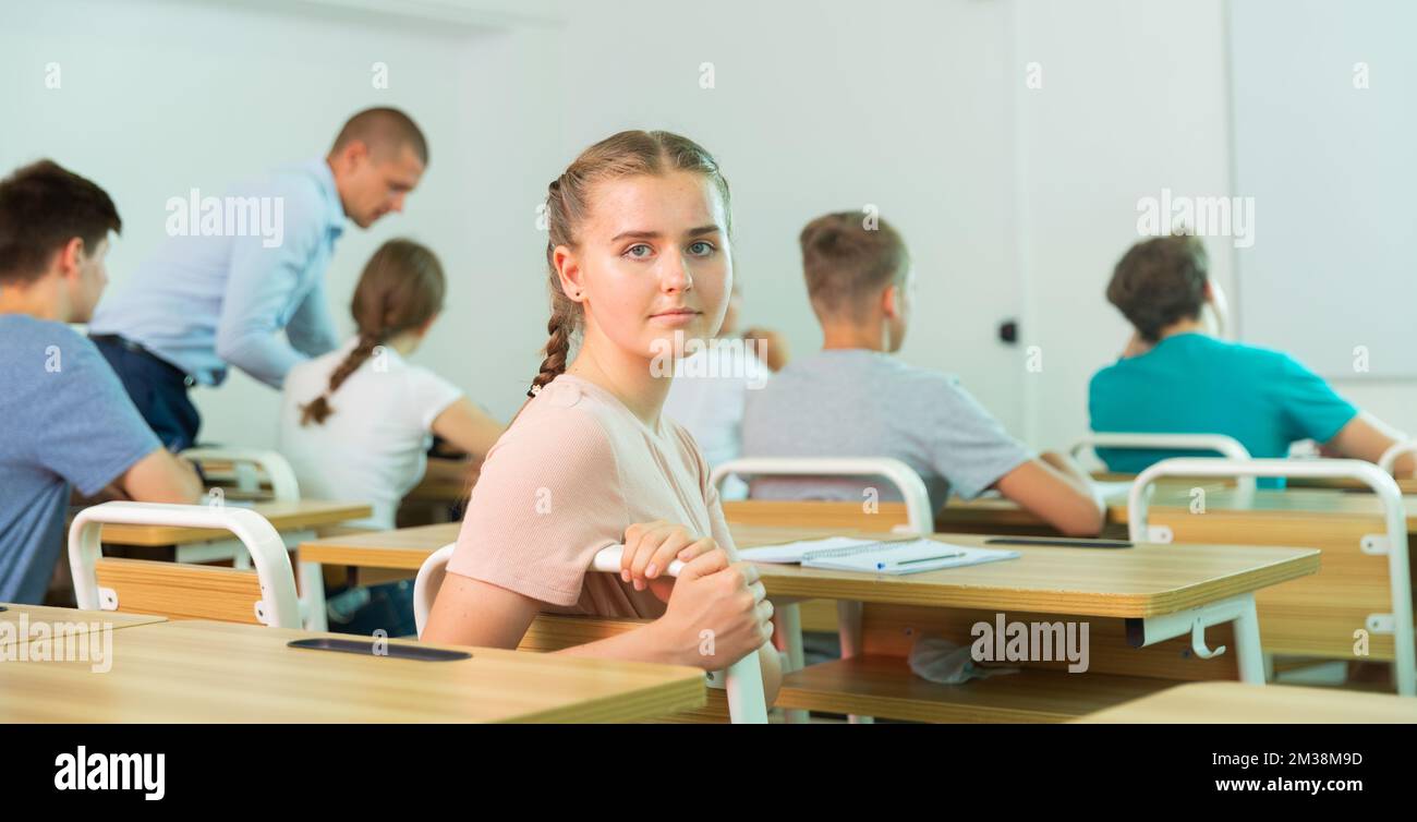 Positive teenage schoolgirl sitting at lesson in classroom Stock Photo ...