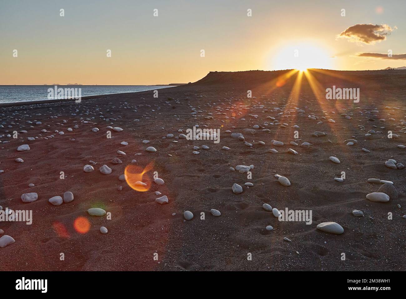 Iceland landscape black sand beach with stones and sunset flare Stock Photo